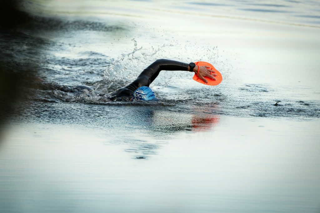 swimrun competitor swimming wearing orange swimrun paddles 
